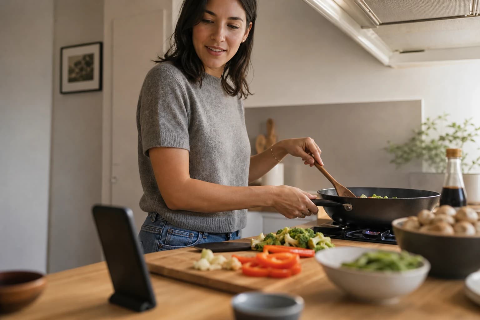 A phone rests by chopped vegetables while dinner cooks in a bright kitchen.